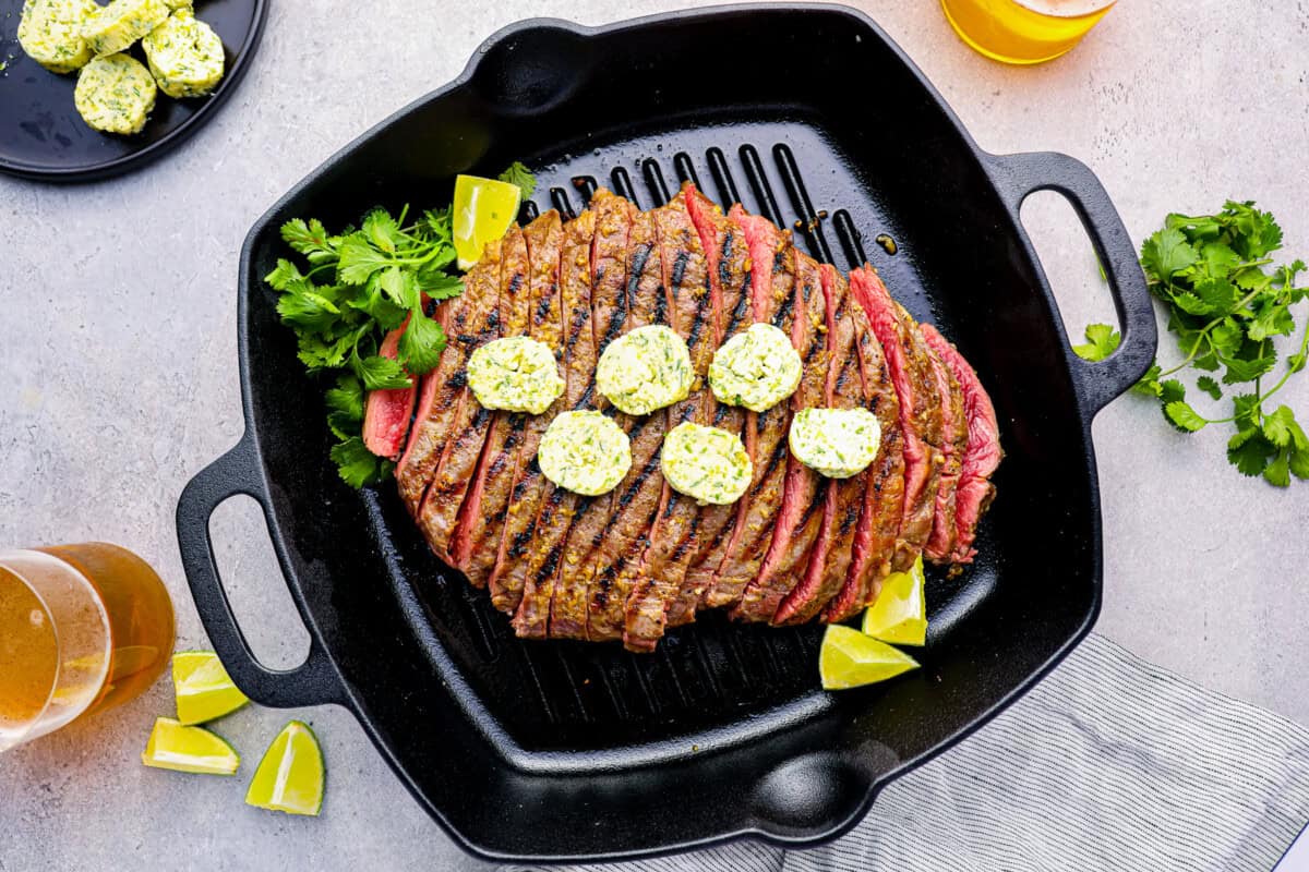 sliced flank steak on a grill pan topped with cilantro lime butter