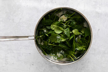 spinach added to parmesan cream sauce in a skillet.