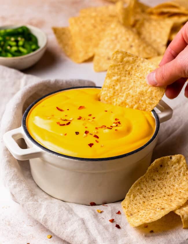 dipping a tortilla chip into a bowl of nacho cheese sauce