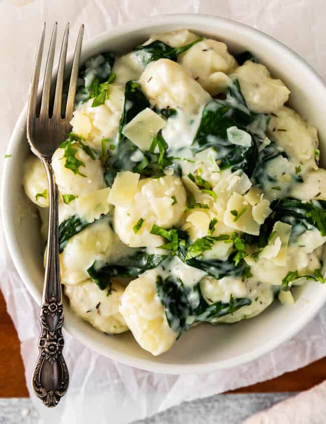 parmesan spinach gnocchi in a white bowl with a fork.