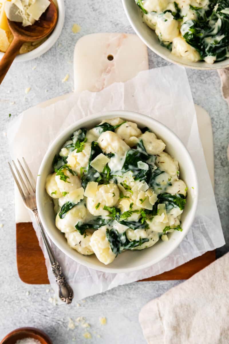 parmesan spinach gnocchi in a white bowl with a fork.