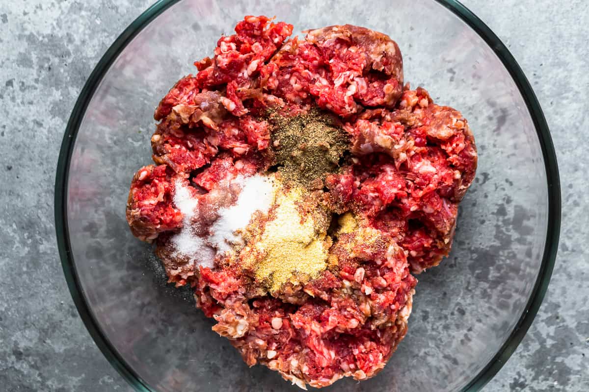 seasoning ground beef in a glass bowl