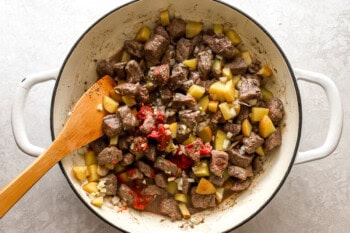 seasoned cubed beef, potatoes, and onions in a pan with a wooden spoon.