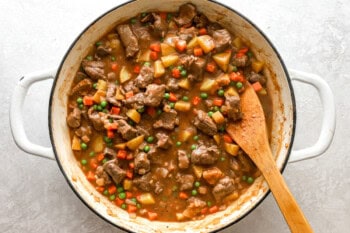 beef pot pie filling in a pan with a wooden spoon.