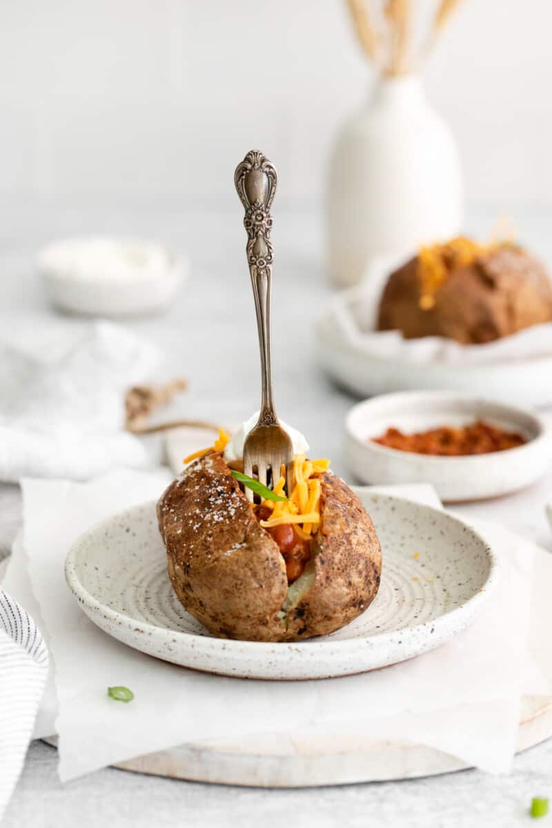 a fork sticking straight up out of a loaded air fryer baked potato on a white plate.