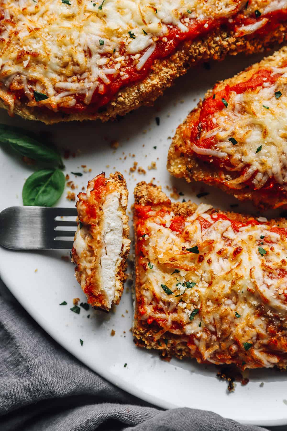 a forkful of air fryer chicken parmesan resting on a platter of air fryer chicken parmesan.