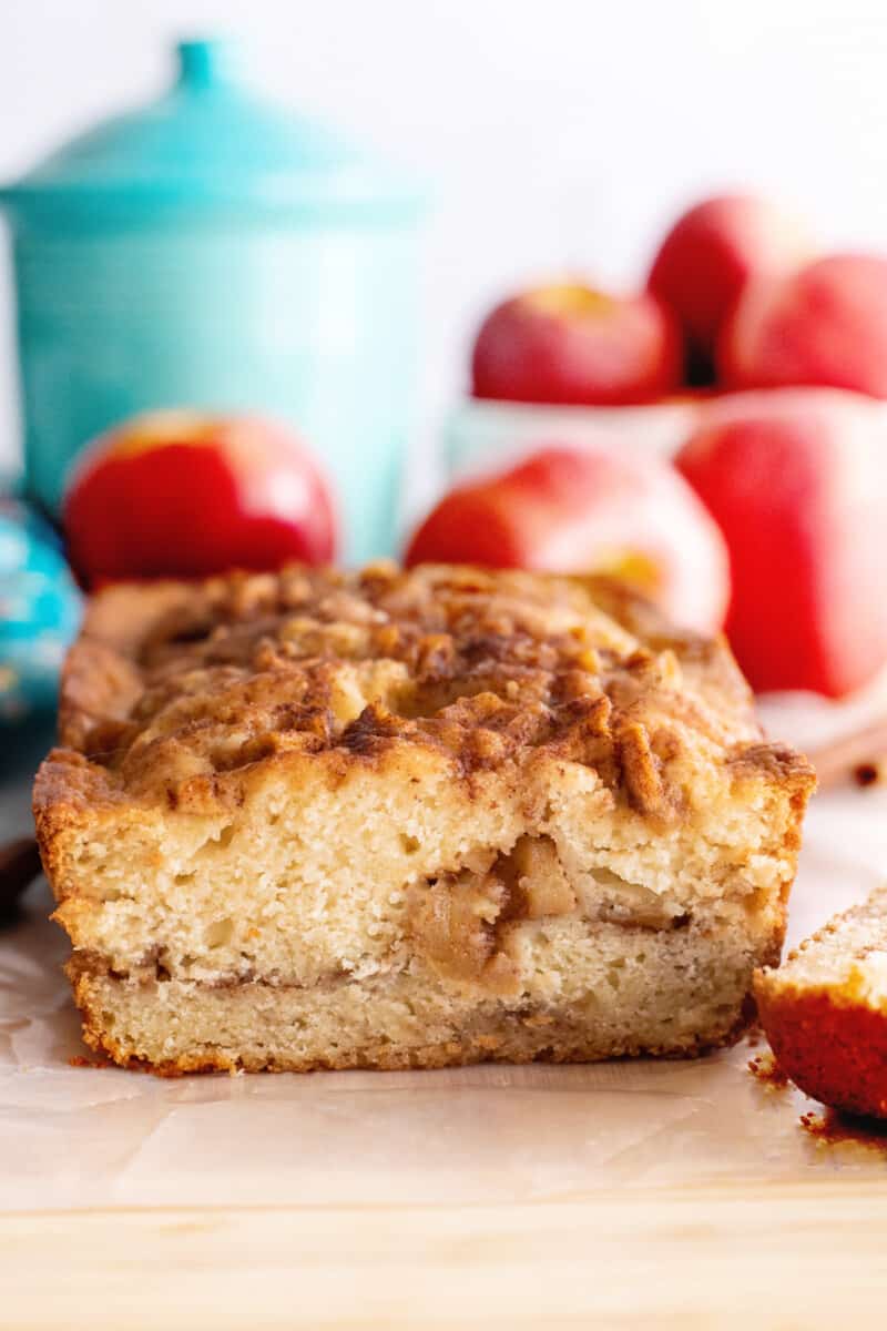 loaf of apple bread on a countertop, with apples out of focus in the background