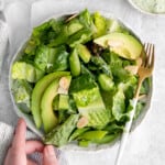 a hand reaching towards a bowl of green salad