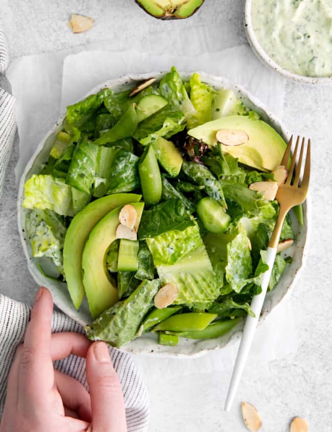 a hand reaching towards a bowl of green salad