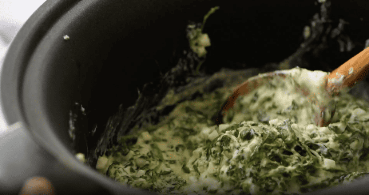 spinach dip in a crockpot with a wooden spoon.