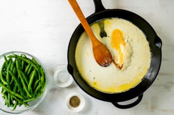 creamed green bean sauce in a cast iron skillet with a wooden spoon.