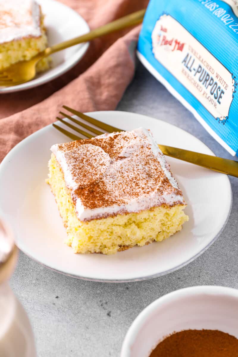 a slice of tres leches cake on a white plate with a gold fork.