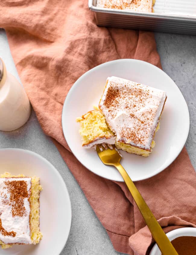 a forkful of tres leches cake resting on a white plate with a slice of tres leches cake.