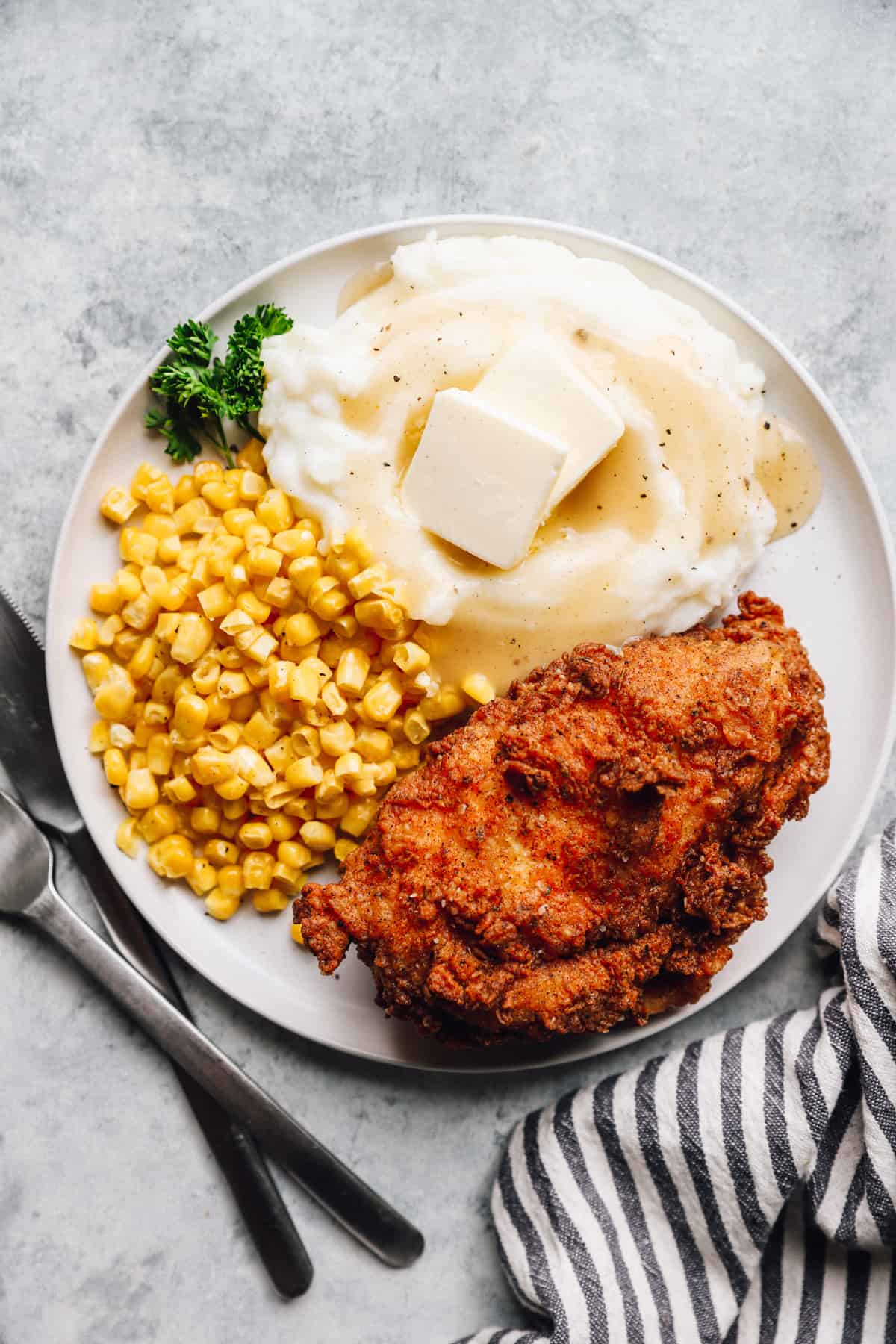 overhead view of a piece of kentucky fried chicken on a white plate with corn and mashed potatoes.