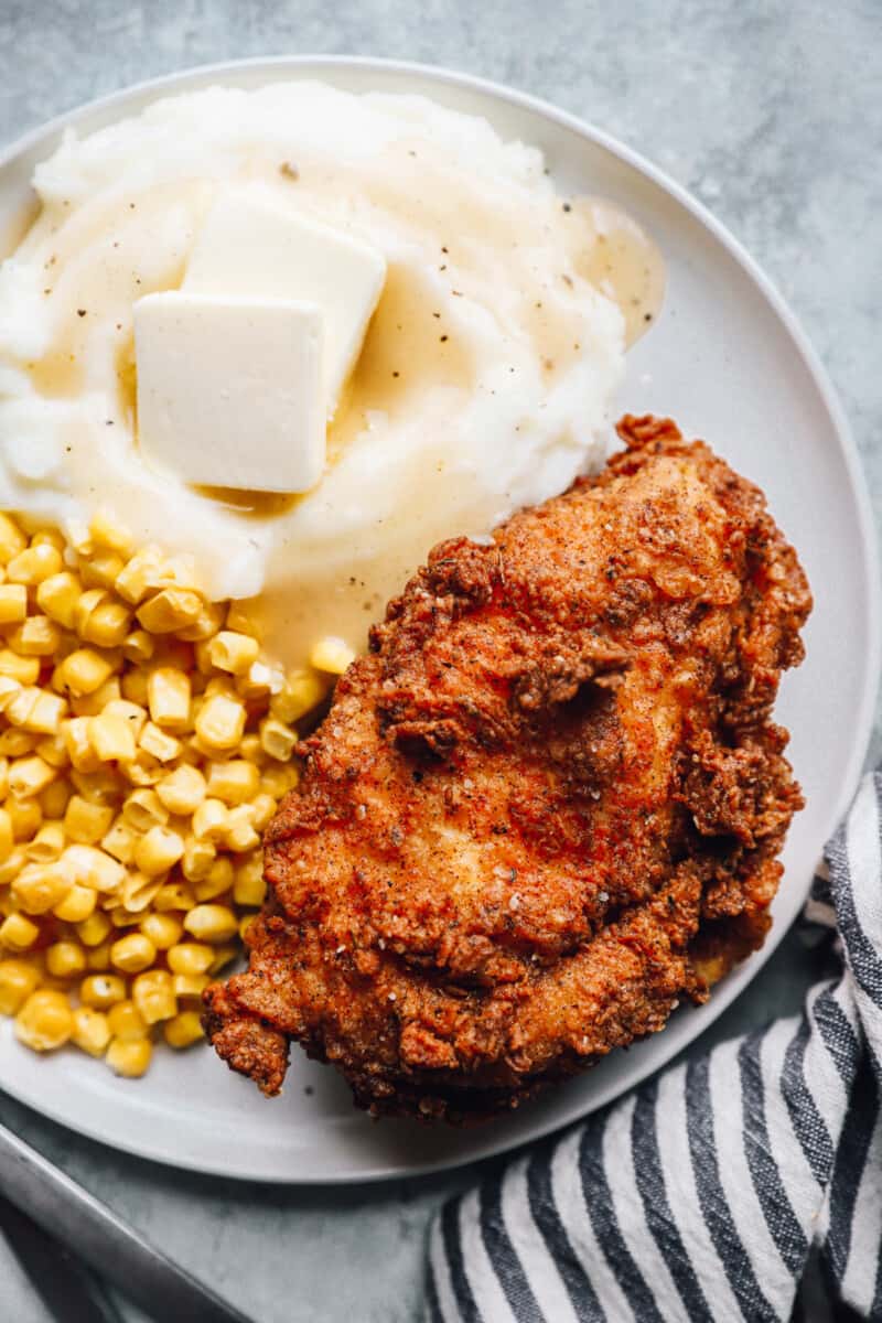 overhead view of a piece of kentucky fried chicken on a white plate with corn and mashed potatoes.