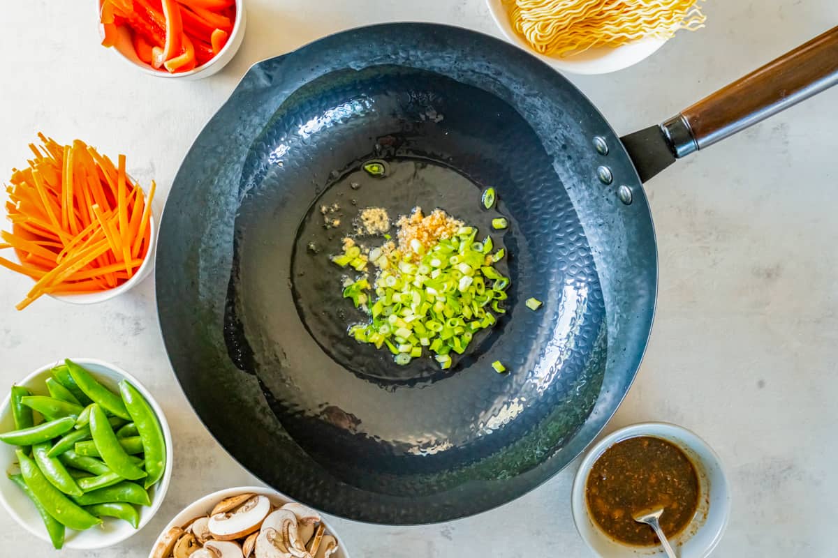 green onions and garlic cooking in oil in a wok.