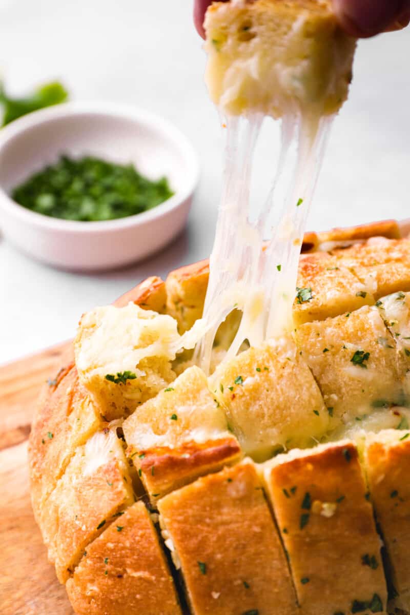 a piece of pull apart cheese bread being removed from a loaf.