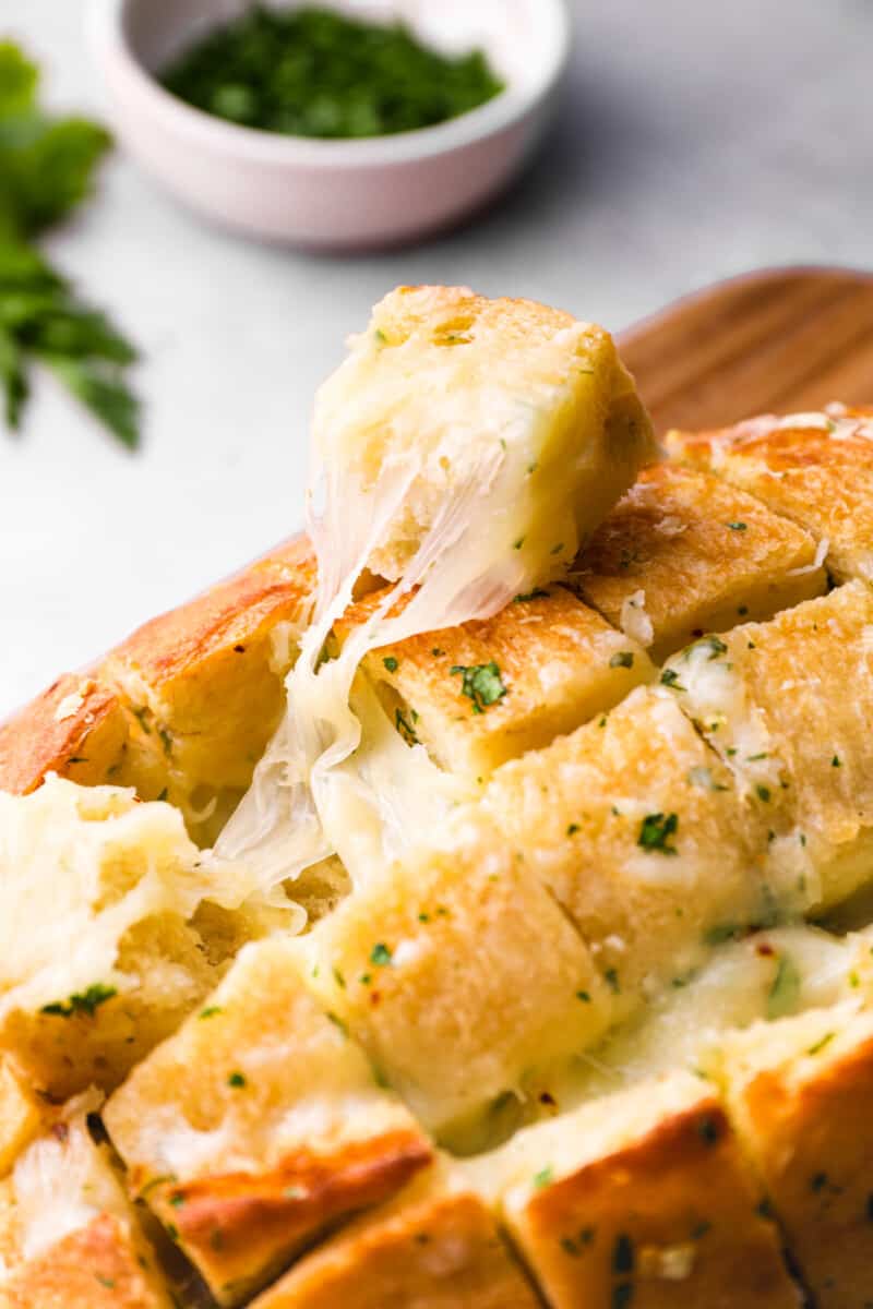 a piece of pull apart cheese bread resting on top of a loaf.