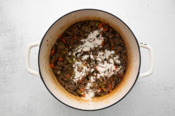 flour sprinkled over sausage and vegetables in a white dutch oven.