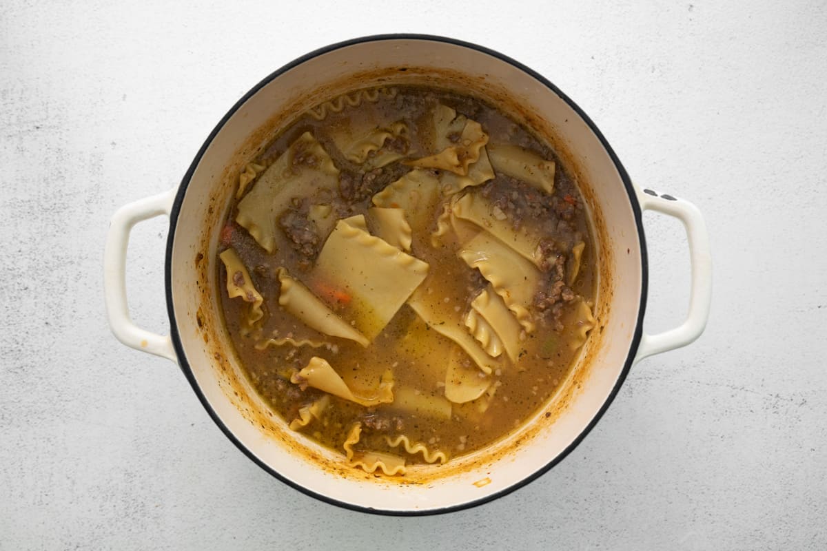 lasagna noodles added to white lasagna soup in a white dutch oven.