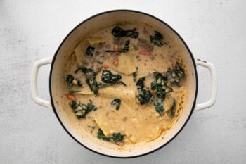 kale added to white lasagna soup in a white dutch oven.