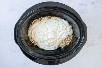 soup mixture poured over chicken and stuffing in a black crockpot.