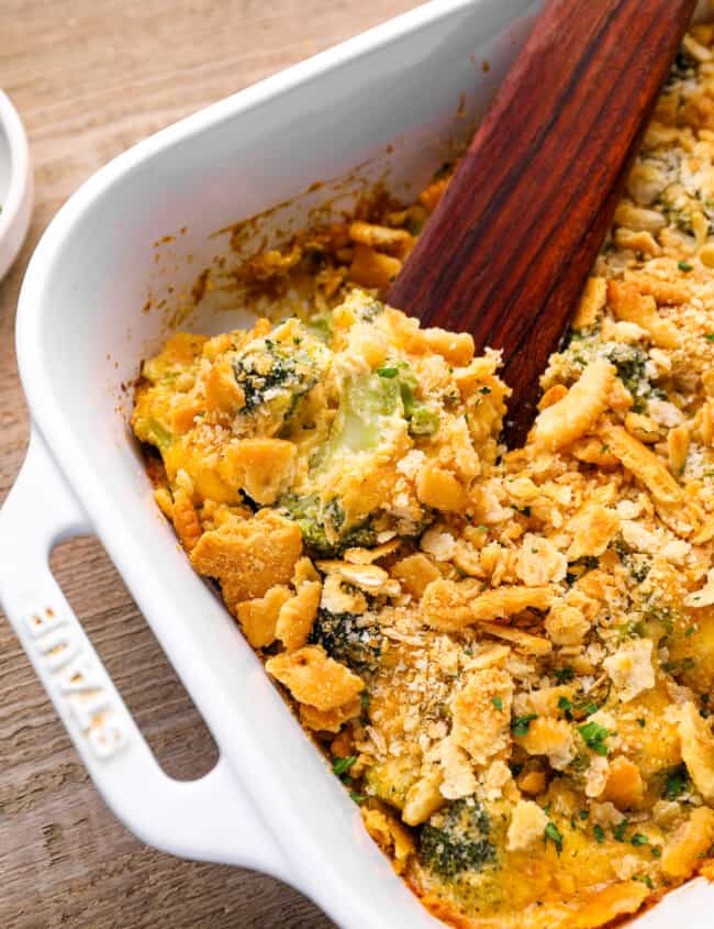 broccoli cheese casserole in a white baking pan with a wooden spoon.