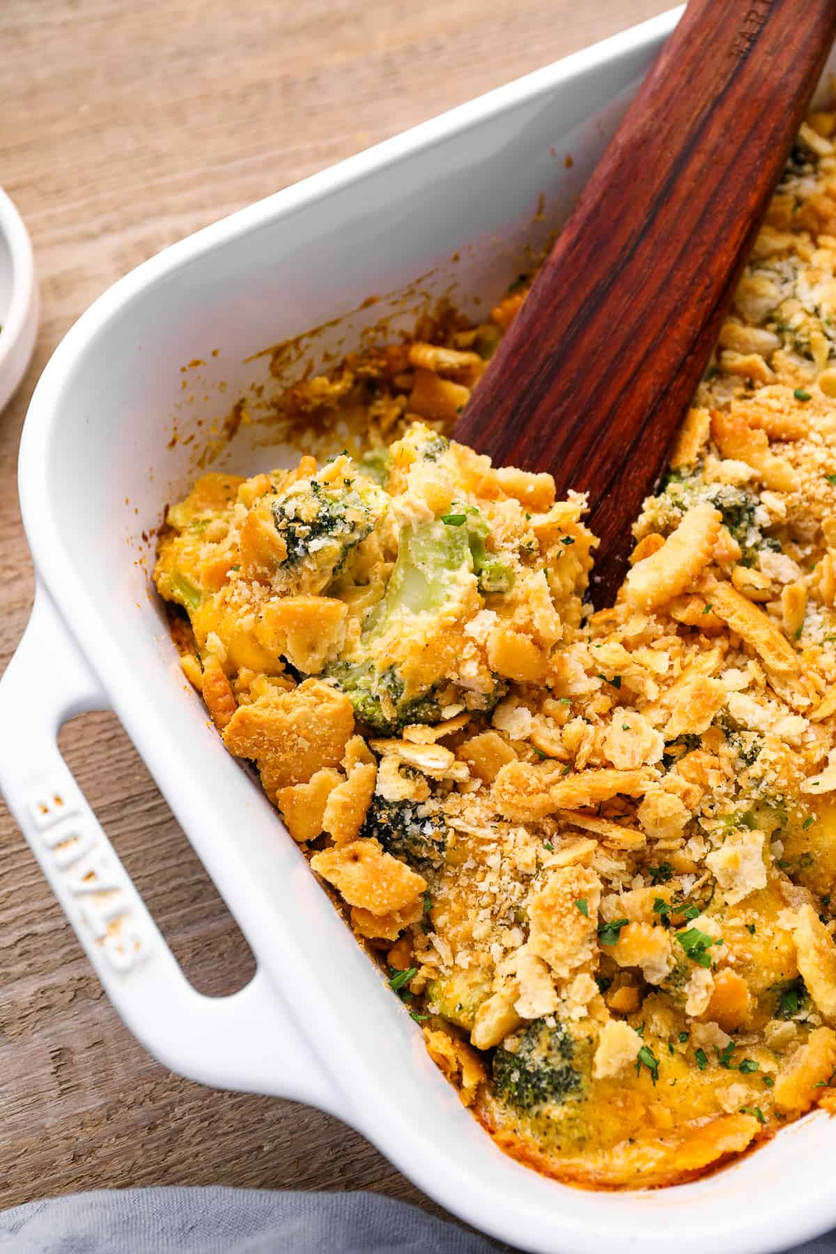 broccoli cheese casserole in a white baking pan with a wooden spoon.