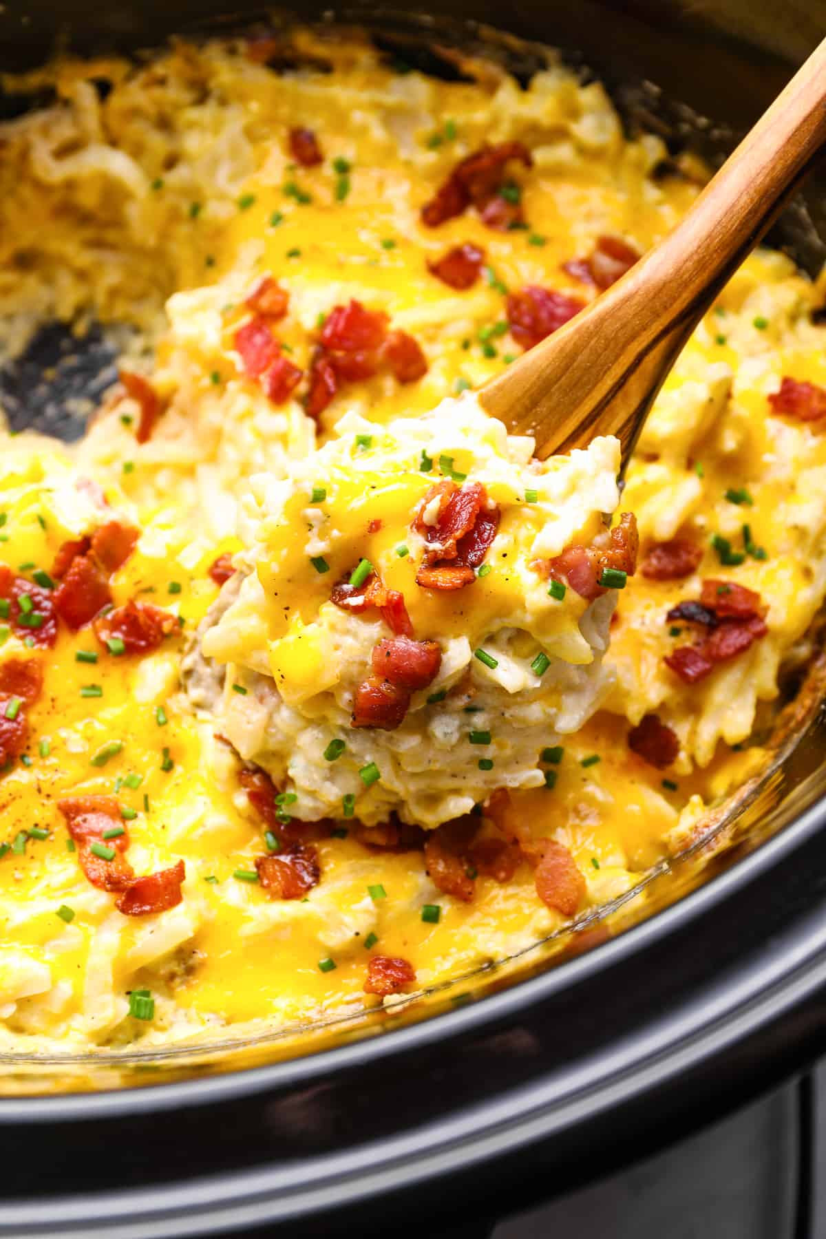 a spoon lifting a scoop of crockpot cheesy potatoes out of a crockpot.