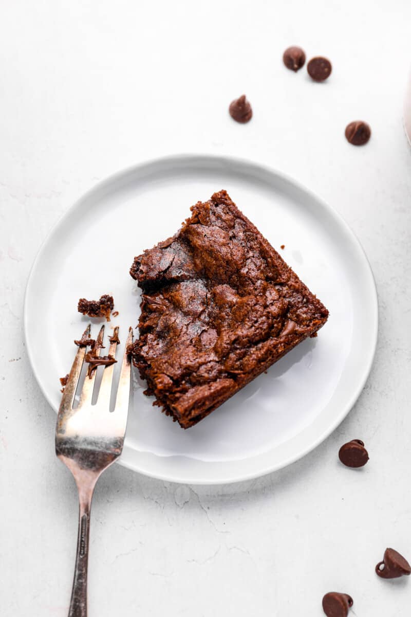 a fork resting on a white plate with a partially eaten brownie.