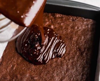 chocolate ganache being spread over cosmic brownies in a baking pan.