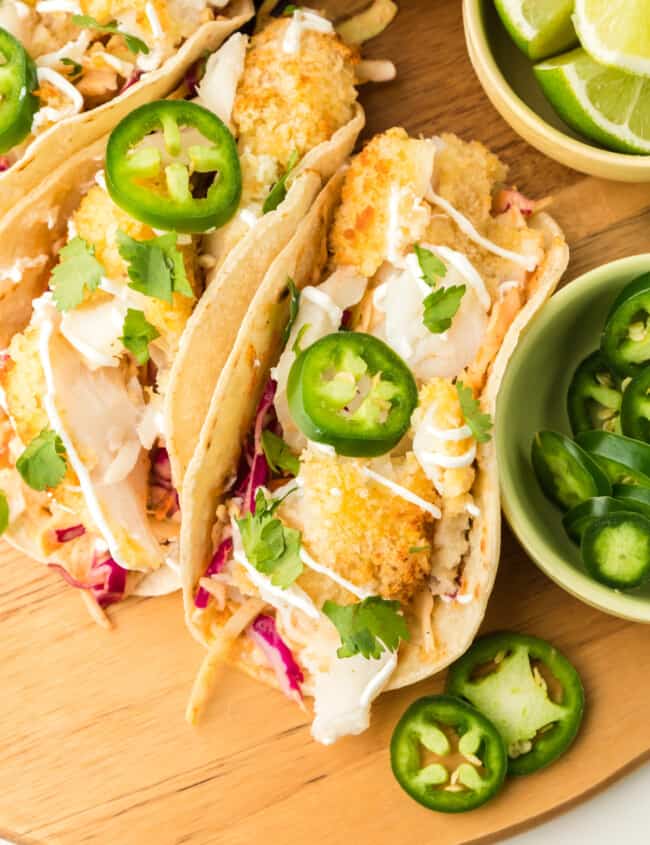 overhead view of 3 air fryer fish tacos on a wooden cutting board with sliced jalapeños.