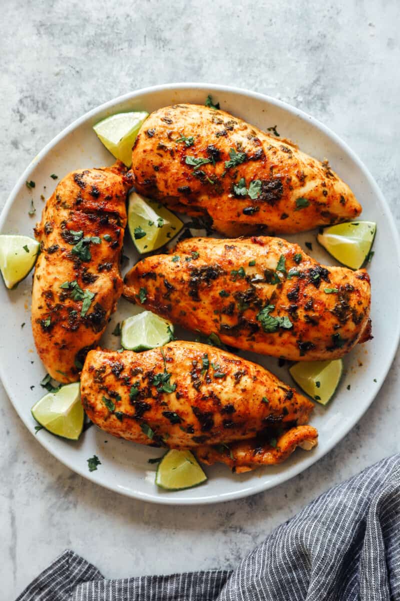 overhead view of 4 cilantro lime chicken breasts surrounded by lime wedges on a white plate.