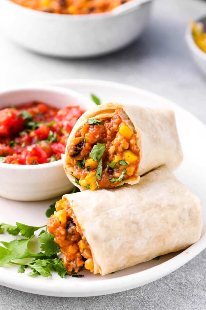 crockpot chicken burrito halves leaning against each other on a white plate with a bowl of salsa.