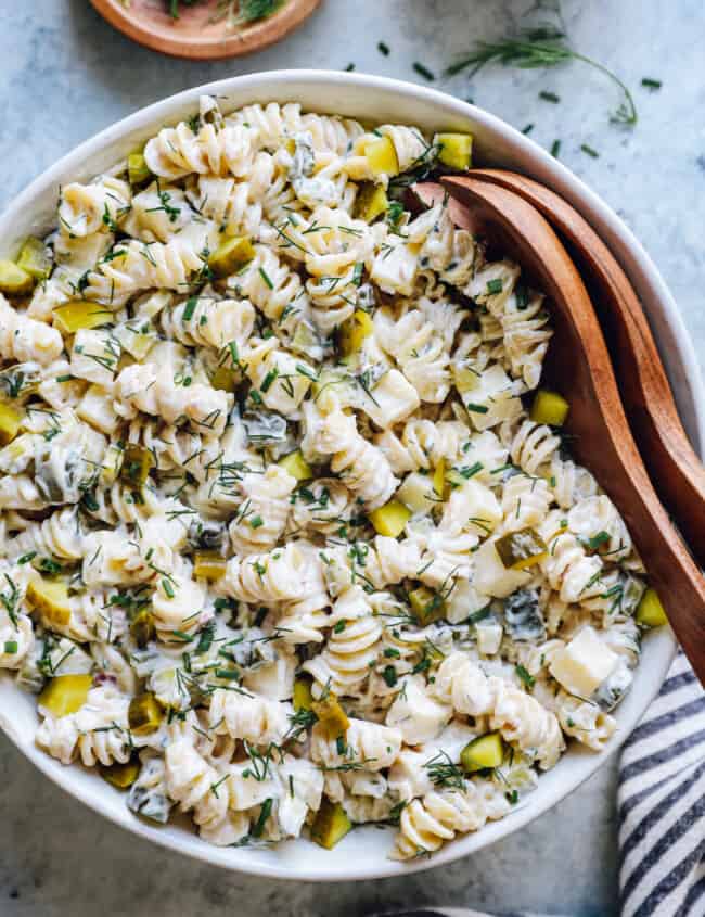 overhead view of dill pickle pasta salad in a white serving bowl with wooden salad tongs.