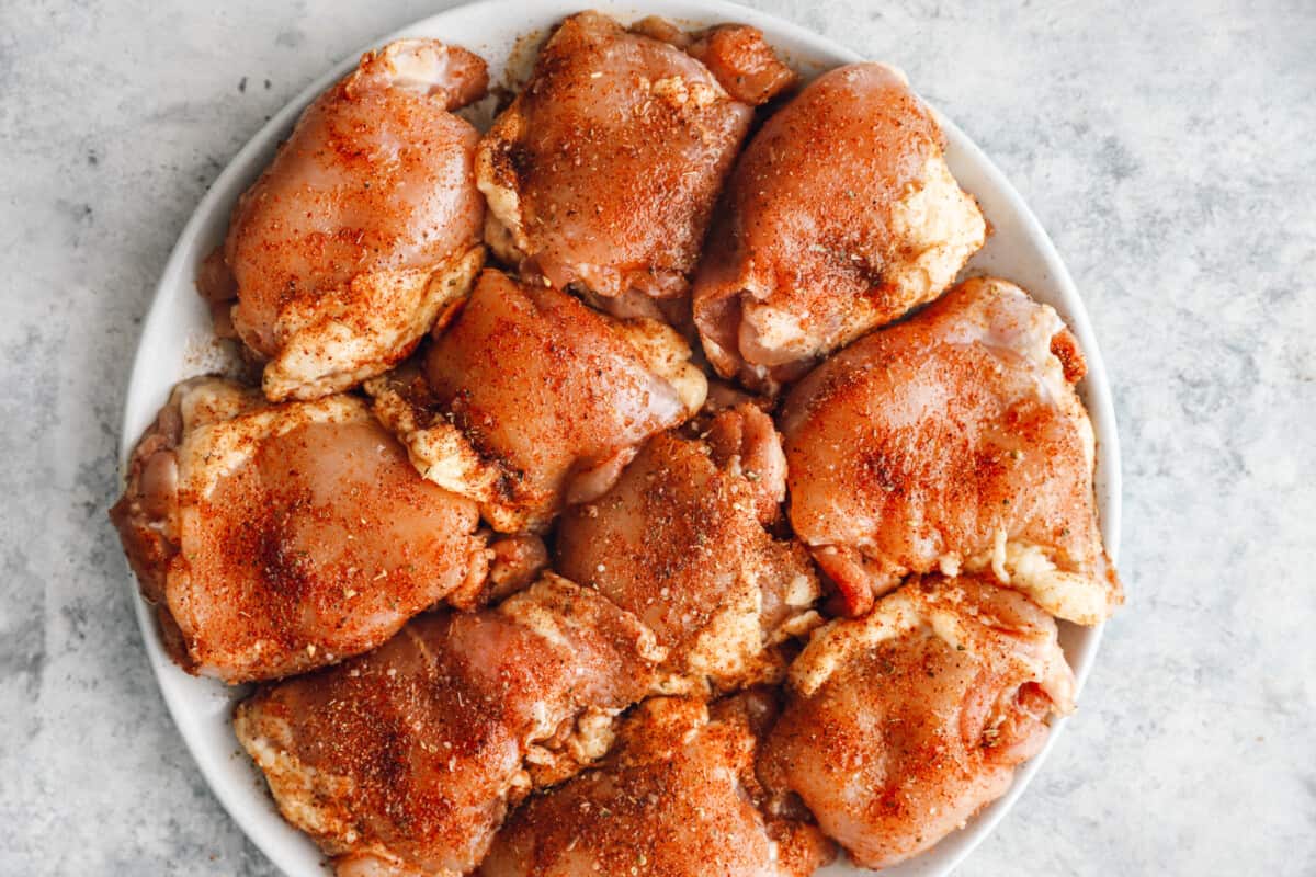 overhead view of seasoned raw chicken thighs on a white plate.