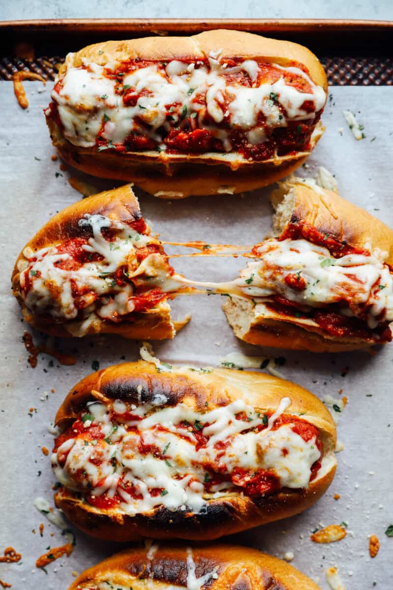 overhead view of meatball subs on a lined baking sheet, one cut in half.