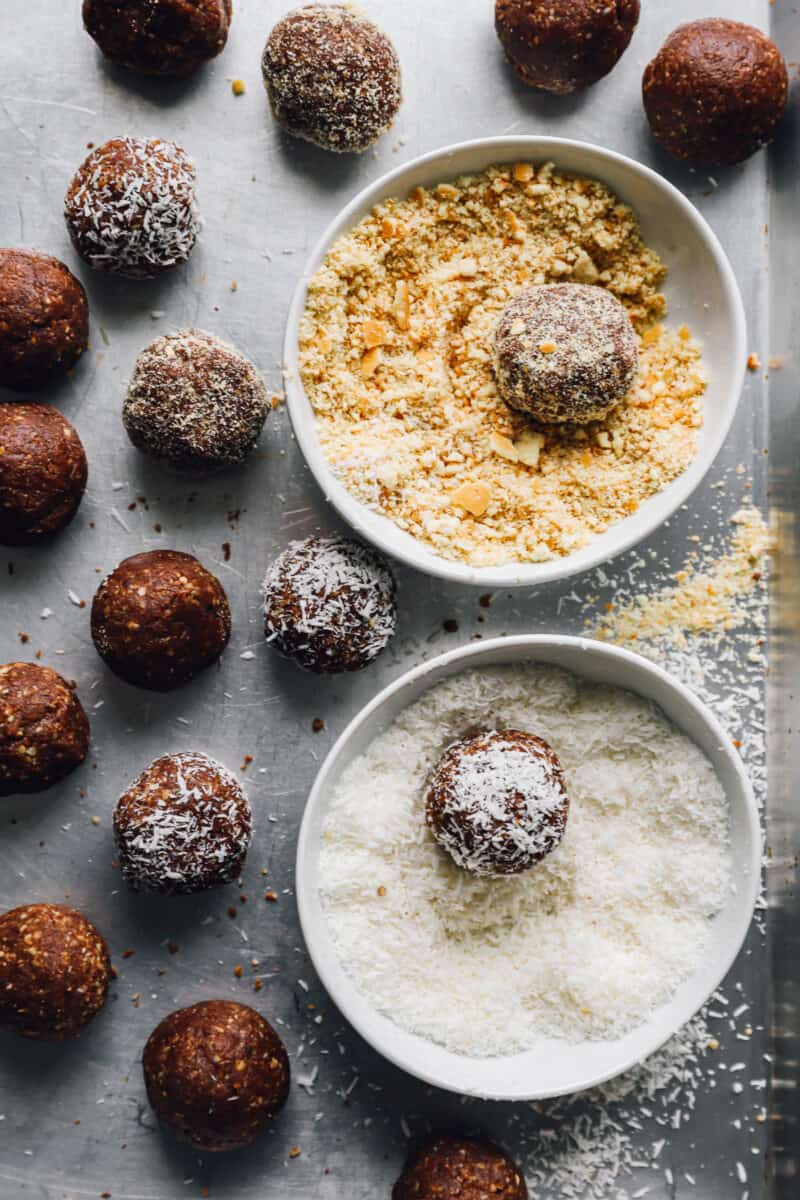 rum balls being coated in toasted coconut and crushed nuts.