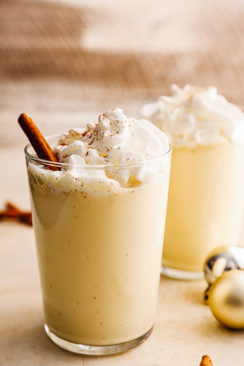 2 glasses of crockpot eggnog with whipped cream and cinnamon sticks.