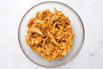 shredded chicken coated in enchilada sauce in a glass bowl.