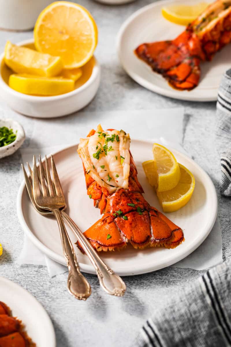 a lobster tail on a white plate with a fork and knife.