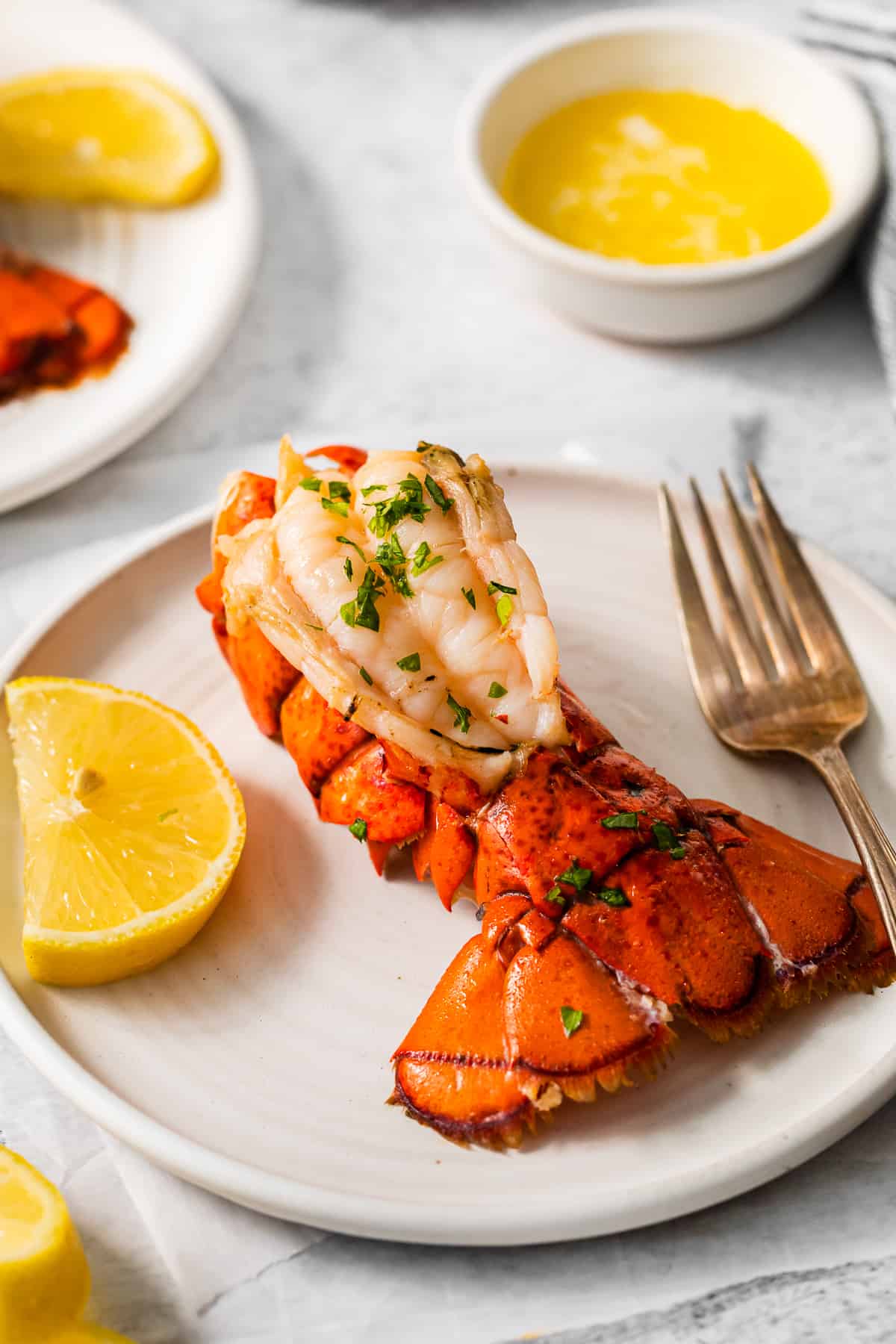 a lobster tail on a white plate with a fork and knife.