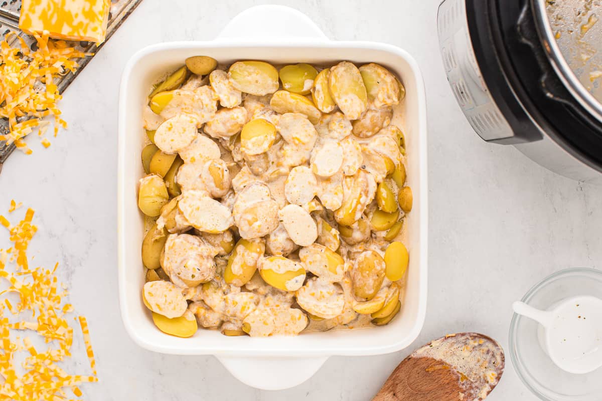 sauce poured over instant pot scalloped potatoes in a white square baking dish.