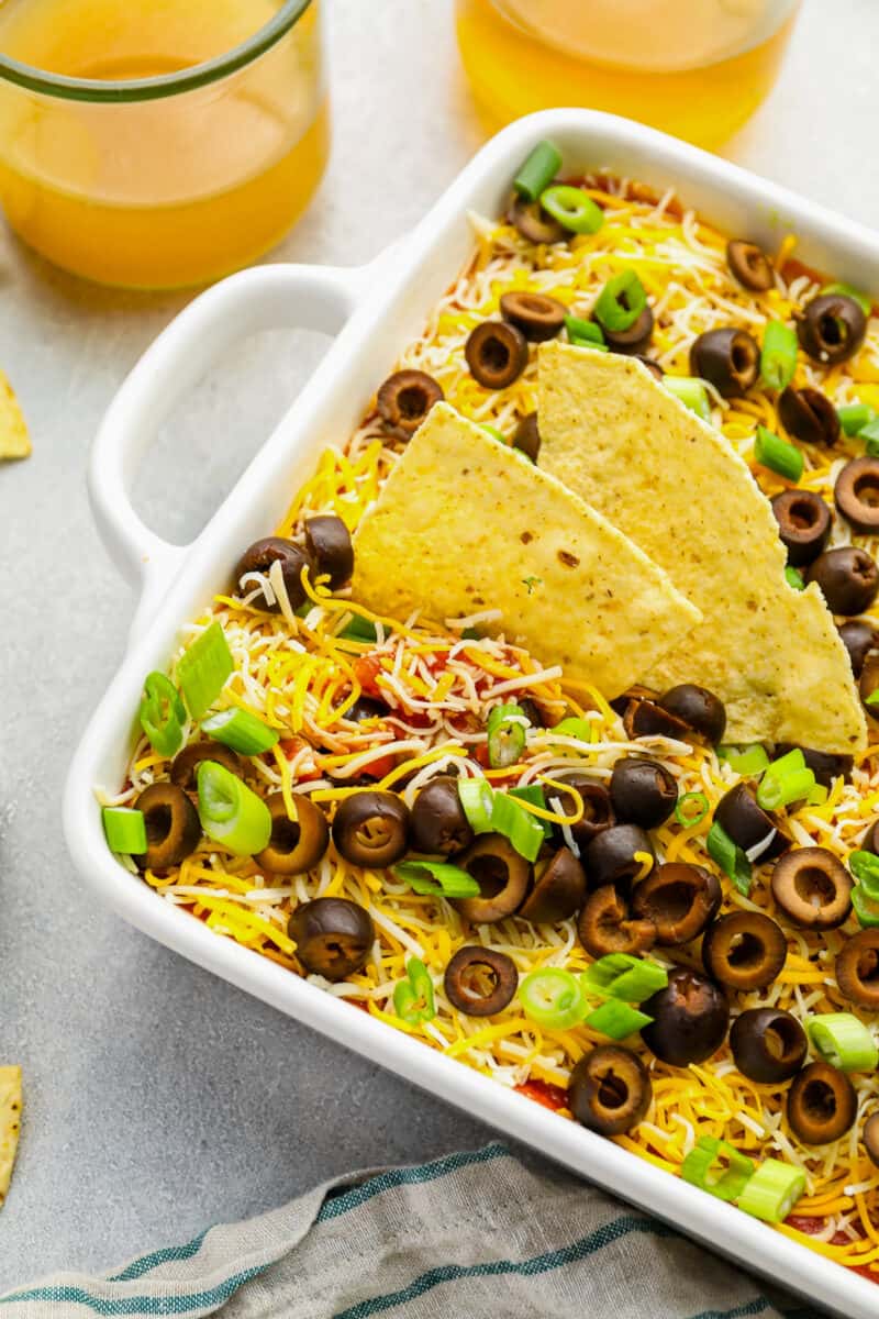 partial view of 7 layer dip in a rectangular baking pan with chips stabbed into it.