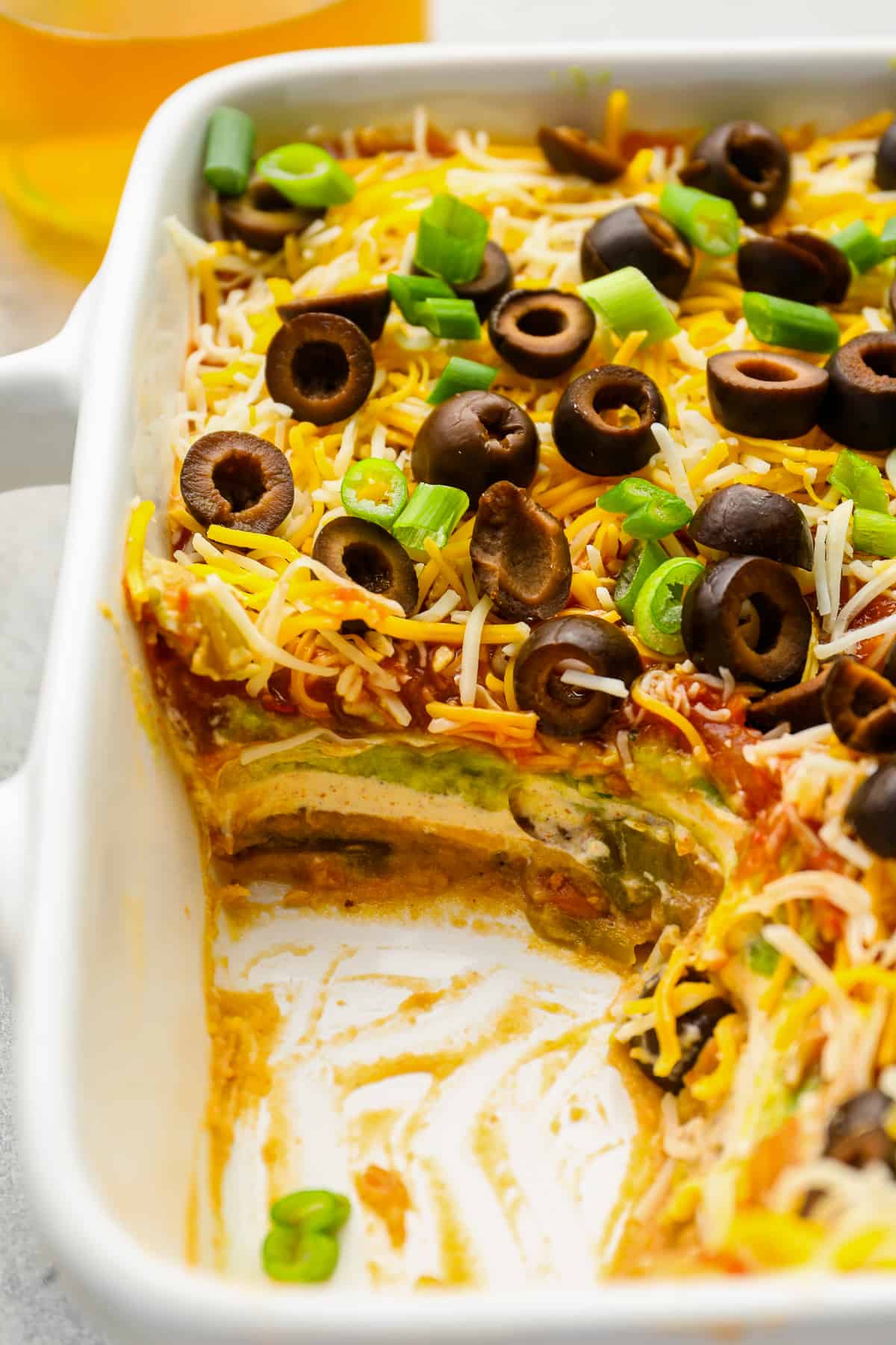 close up of partially eaten 7 layer dip in a rectangular baking pan.