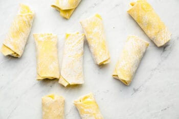 9 uncooked reuben egg rolls on a marble table.