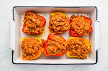 6 bell pepper halves stuffed with ground beef and rice mixture in a white rectangular baking pan.