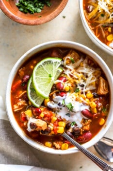 overhead view of a bowl of 7 can soup with lime wedges, cheese, and a spoon.