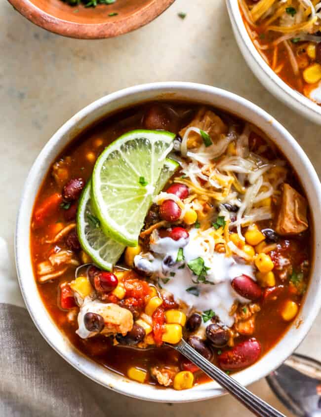 overhead view of a bowl of 7 can soup with lime wedges, cheese, and a spoon.