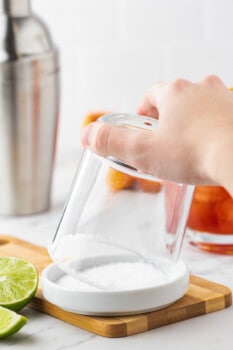 an upturned short rocks glass being dipped into slat to create a rim.